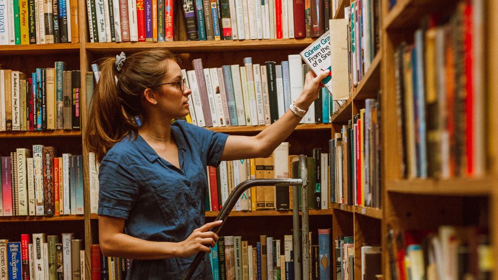 一位女士在图书馆蓝色书架上摆放书籍的照片。 